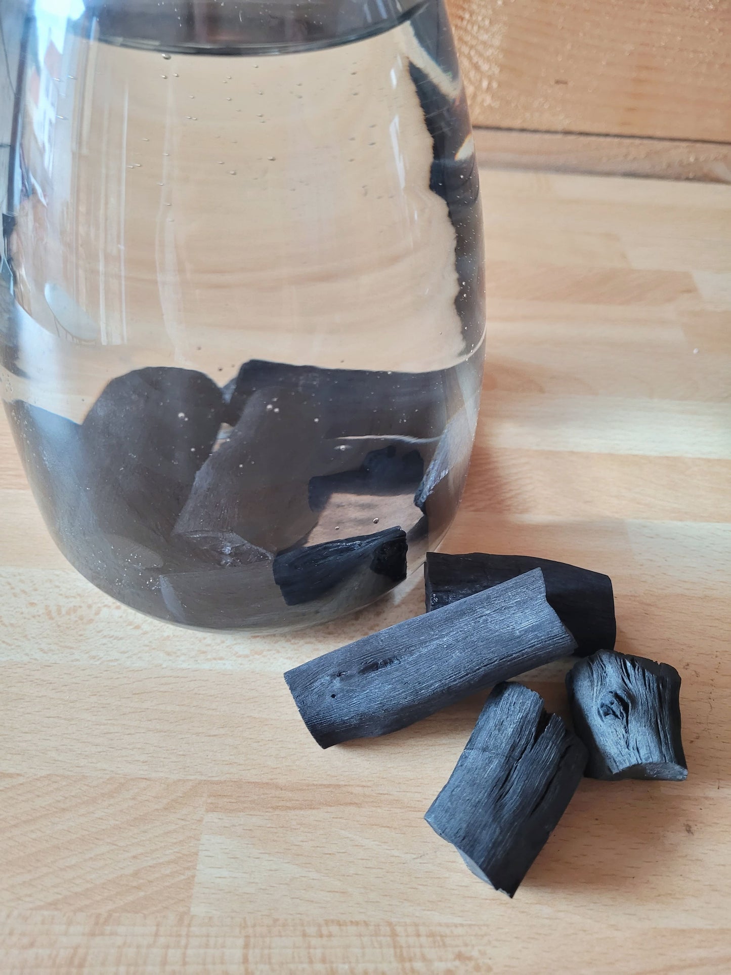carafe d'eau avec batons de charbon à l'intérieur et posés devant